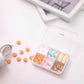 Sealed mini pill box open with grid compartments filled with multicolored tablets