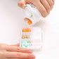 Hands holding a white pill box open, revealing divided compartments with tablets