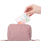 Mini pill box with clear lid partly open placed above a pink zip pouch