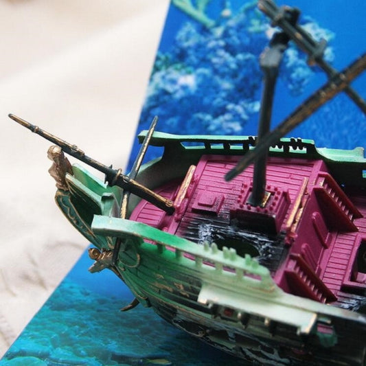 Close-up toy shipwreck aquarium ornament with green hull and pink deck details