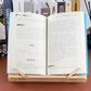 Wooden book stand holding an open book with metal clips, light natural wood frame