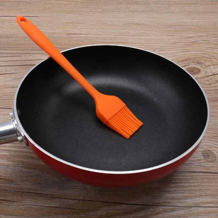 Orange silicone oil brush for skillet use, with fan bristles and sturdy handle.