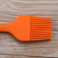 Orange silicone basting brush with wide fan bristle head and short handle grip.