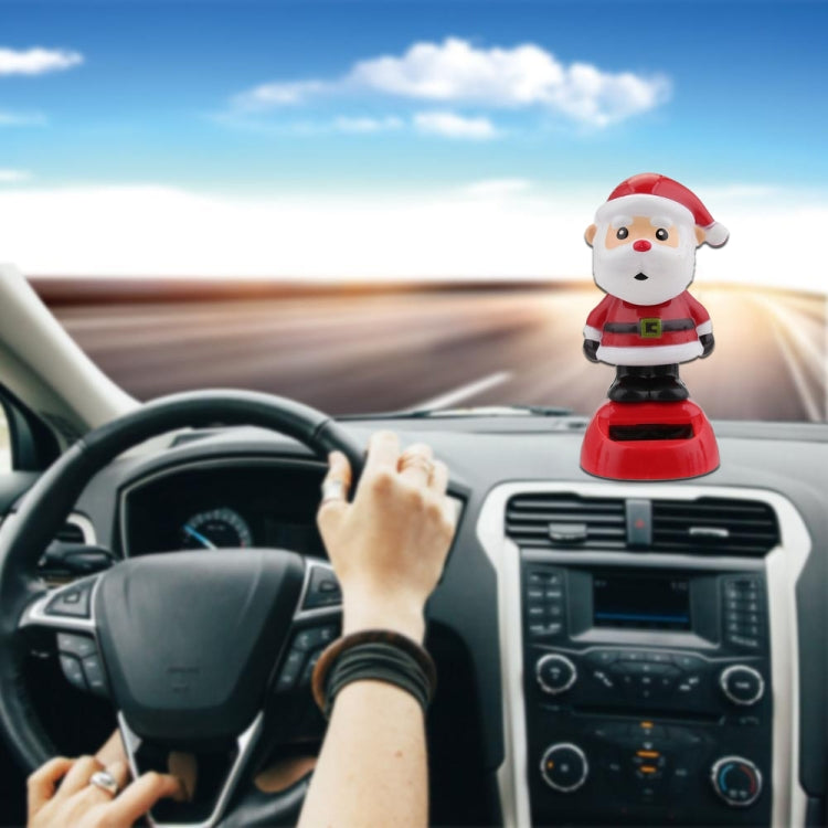 Small Santa Claus solar decoration standing on red base on a car dashboard