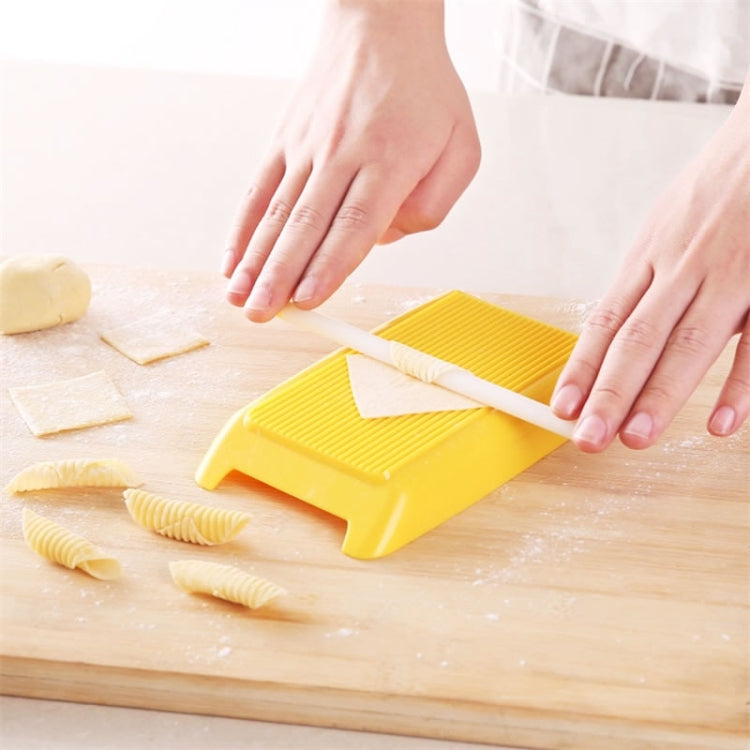 Yellow plastic spaghetti pasta mold with ridged surface, forming shaped pasta on a board
