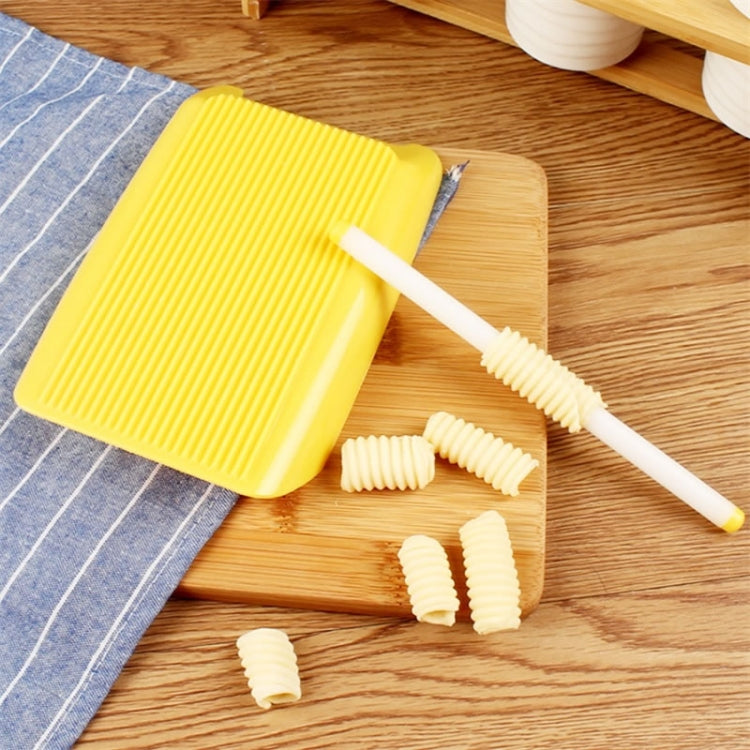 Yellow ridged pasta mold and white roller with formed ridged macaroni on a wooden board