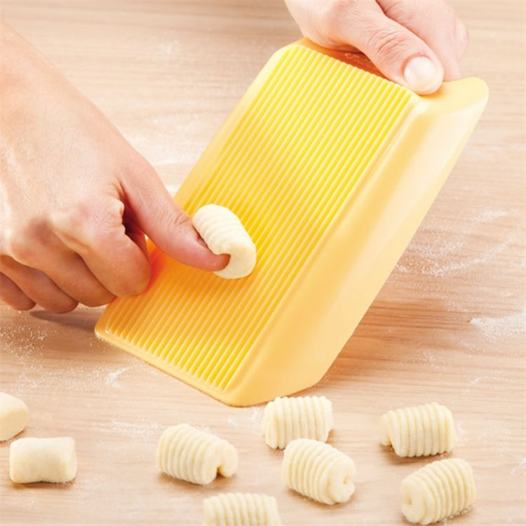 Hands pressing dough into yellow plastic ridged spaghetti mold, with shaped pasta pieces