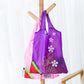 Purple reusable folding grocery shopping bag hanging with flower appliques and green-trim pocket