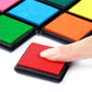 Red square ink pad on black base, finger pressing into textured sponge