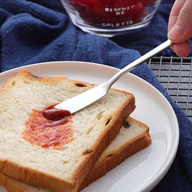 White butter knife with a long handle, spreading bread on a plate.