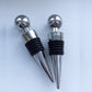 Set of two round wine bottle stoppers with chrome ball tops and black ribbed seals