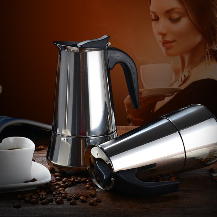 Stainless steel moka coffee maker pot with black handle, coffee cups nearby