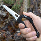 Black D-ring carabiner multitool keychain with serrated blade held in hand.