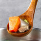 Wooden spoon lifting chopped vegetables, cheese, and meat from a pot