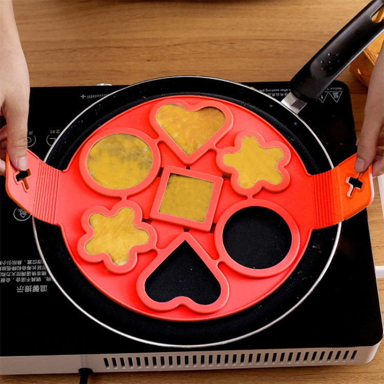 Red silicone egg ring mold on skillet, creating multiple shaped fried eggs