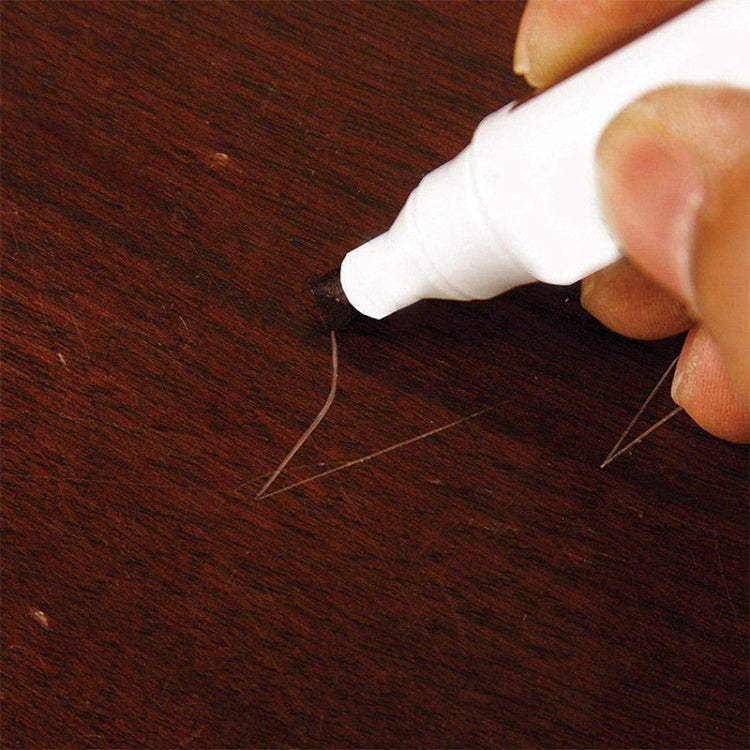 Hand using a white-capped furniture touch-up marker pen on dark wood surface