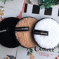 Three round microfiber cleansing puffs—black, beige, and white with black labels.