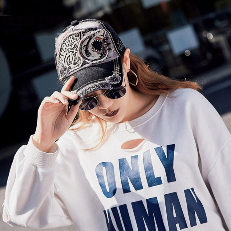 Black baseball cap with shark embroidered patch, worn with sunglasses and hair visible.