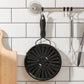 Perforated black stovetop heat plate with hanging loop, displayed on kitchen wall