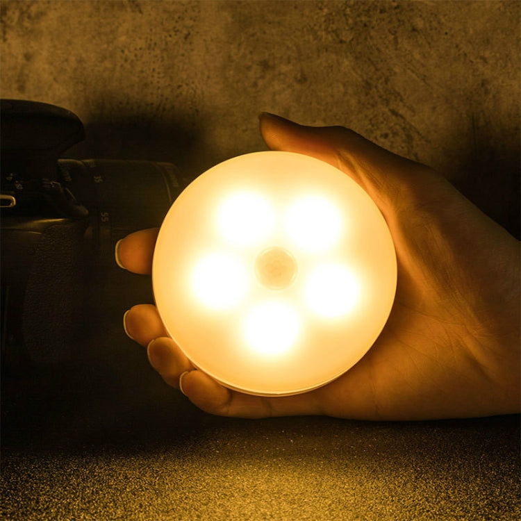 Round LED night light with warm amber glow, held in a hand