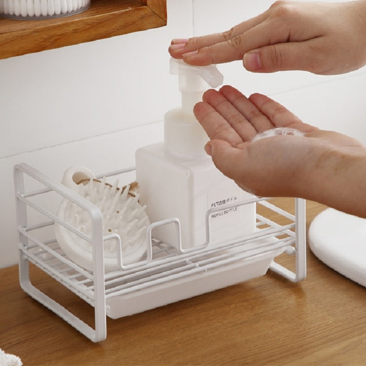 White metal dish drain rack with soap dispenser and brush holders, hands adjusting