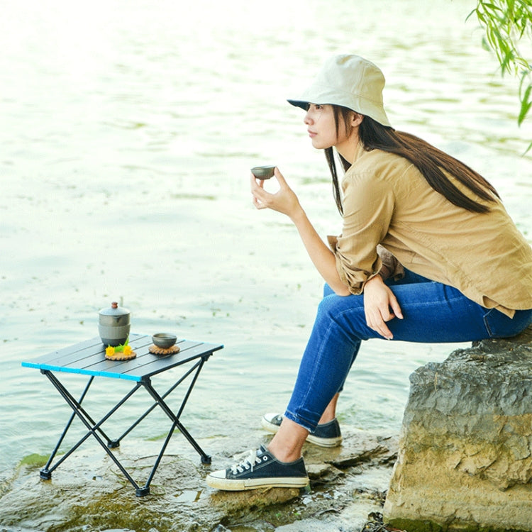 Portable folding camping table in use outdoors near water, black tabletop with blue trim