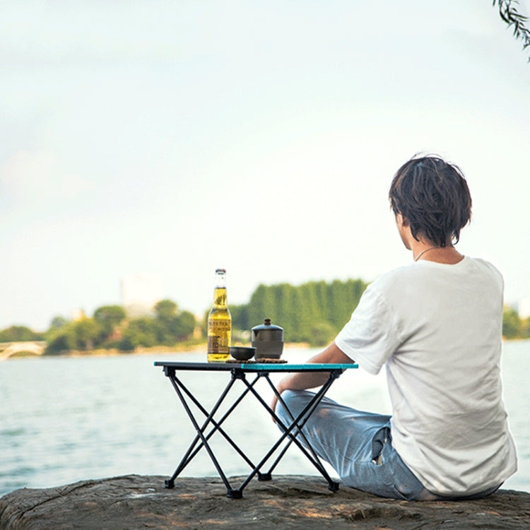 Folding camping table with drinks and cookware on black slatted top; black X-frame legs