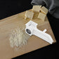 Plastic hand-crank rotary grater producing cheese shavings on cutting board