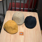 Three newsboy caps: black, cream, and mustard, with curved brims