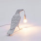 Gray bird shaped table lamp leaning forward with warm glowing bulb and cord