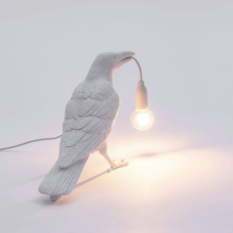 Gray bird shaped table lamp leaning forward with warm glowing bulb and cord
