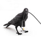 Black bird shaped lamp with glowing bulb near feet and arched wire connection