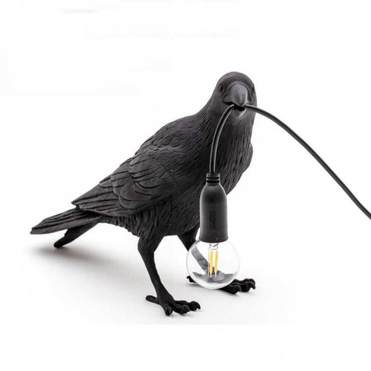Black bird shaped lamp with glowing bulb near feet and arched wire connection