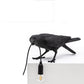 Black bird wall lamp resting on a ledge with glowing bulb and hanging cord