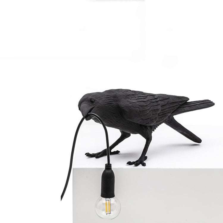 Black bird wall lamp resting on a ledge with glowing bulb and hanging cord