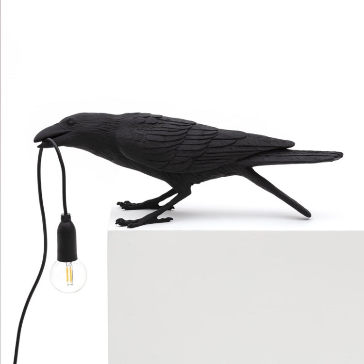 Black bird table lamp on white base with glowing E14 bulb