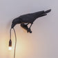 Black resin bird wall lamp with warm bulb and long cord, bird perched on mount