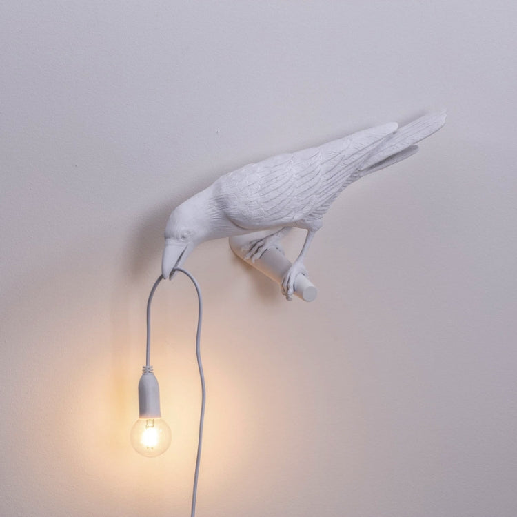White resin bird wall lamp with glowing bulb, curved mount, and dangling cord