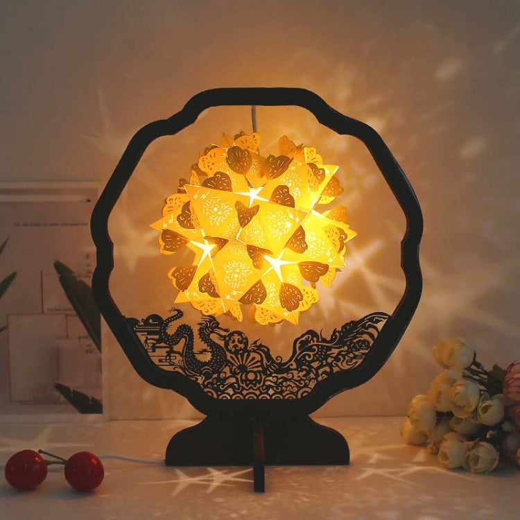 Paper carving shadow lamp on black stand, yellow floral paper shade glowing