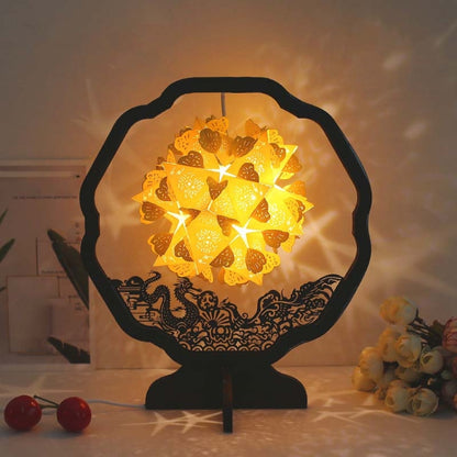 Paper carving shadow lamp on black stand, yellow floral paper shade glowing