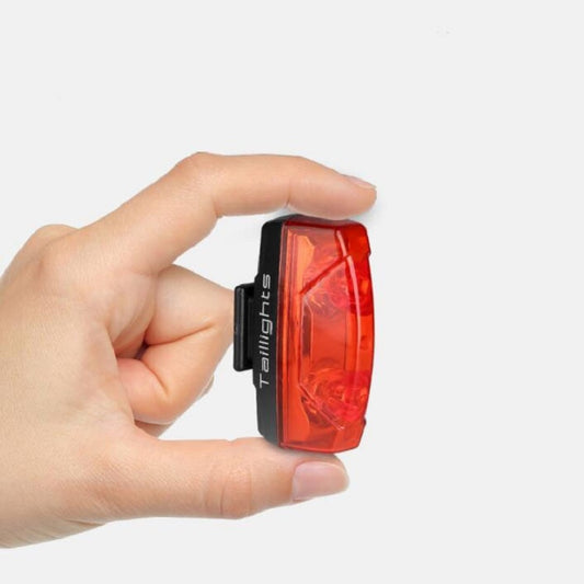 Rear bike taillight held in hand, showing red lens and black side clip