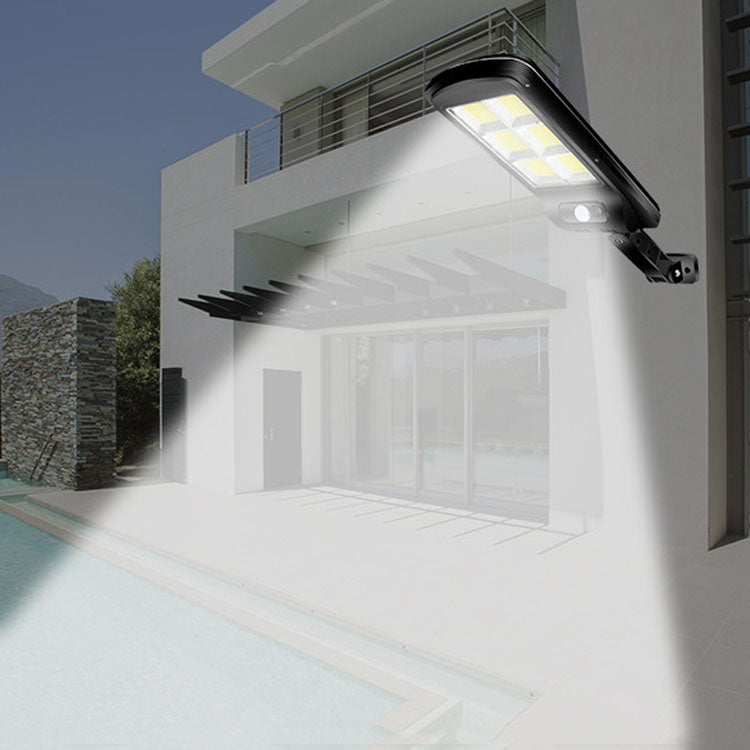 Black solar street light mounted under an eave, casting a bright motion beam