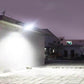 Solar street light illuminating a paved courtyard walkway from a wall-mounted head