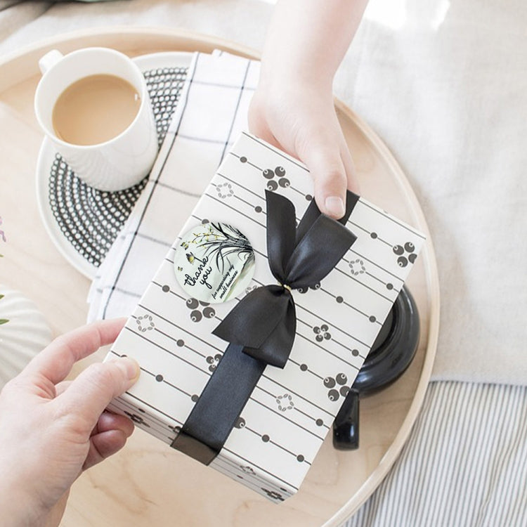 Hands placing flower thank-you sticker on wrapped gift with black bow