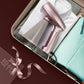Rose-pink mini handheld garment steamer on folded fabric with connected power cord