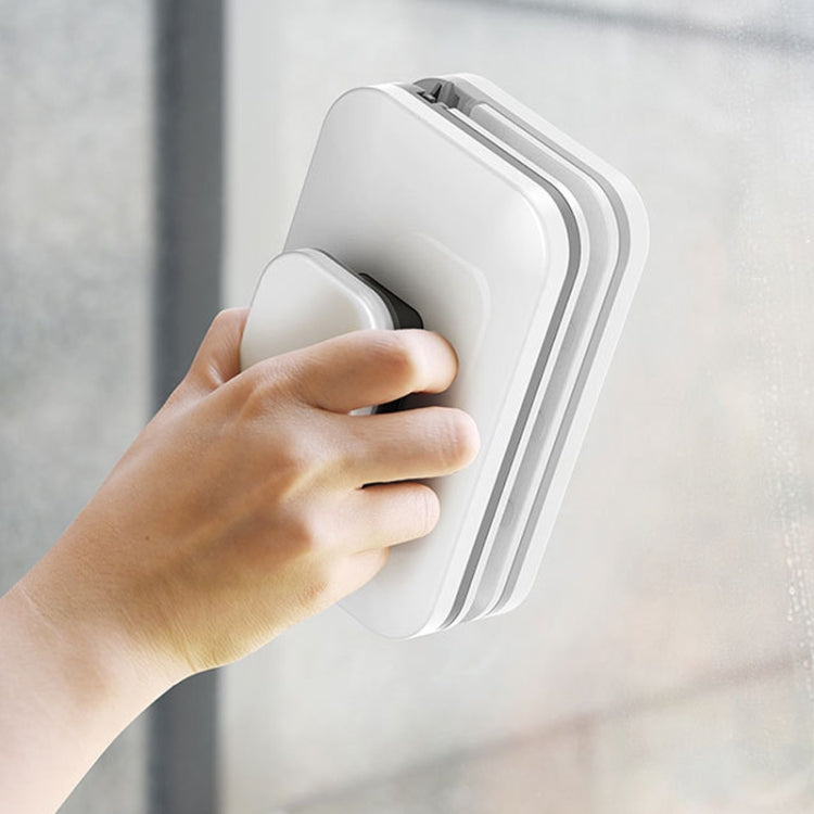 Magnetic window wiper held against glass, rectangular white and gray body with grip tab