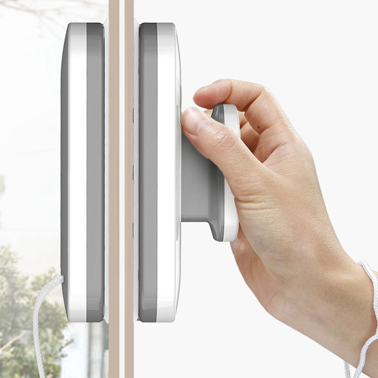 Double-sided magnetic window wiper with gray handles, shown on window edge with hand