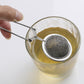 Stainless steel mesh sphere infuser placed in a clear cup, long tongs handle
