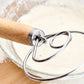 Oak-handled coil whisk stirring pale dough in a glass bowl