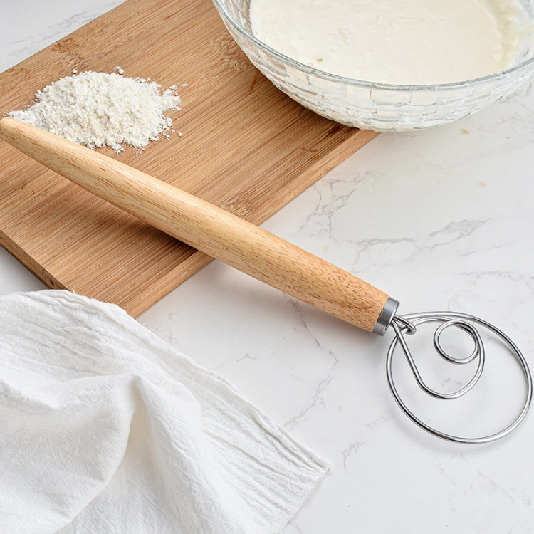Oak-handled coil whisk resting on a cutting board near flour